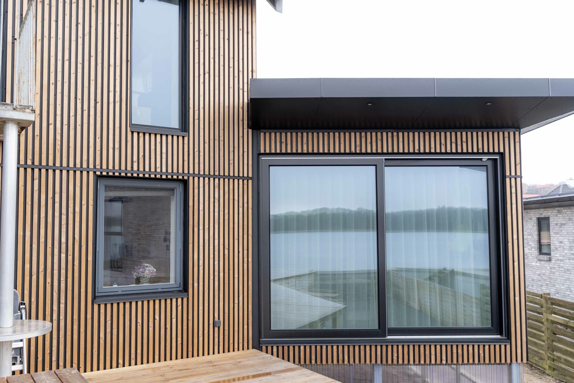 Facade with vertical Aluwood slats and a large black sliding window reflecting the fjord
